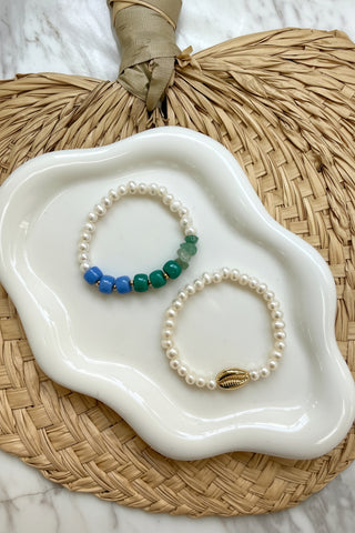 Two pearl bracelets on a white dish with a woven mat background