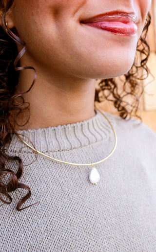 Close-up of a person wearing a gold necklace with a pendant. Taudrey Jewelry, Tidal Cuff Necklace